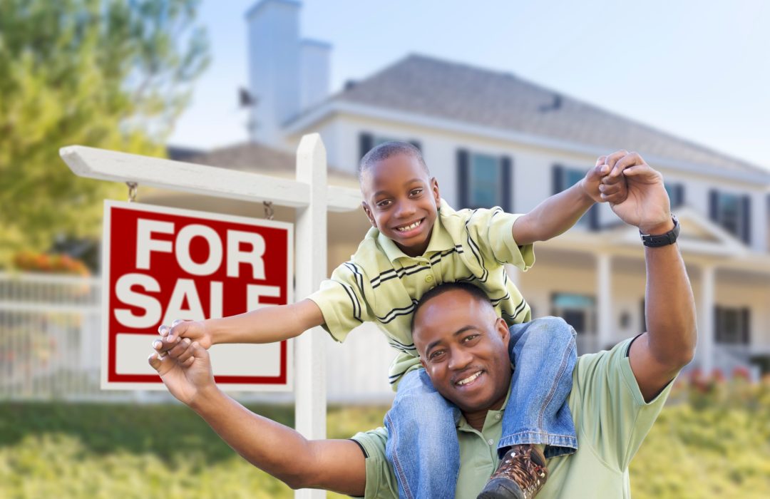 Happy African American Father and Son in Front of Home and For Sale Real Estate Sign.